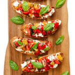 Burrata Bruschetta with tomato basil topping on a wooden board.