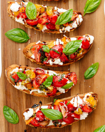 Burrata Bruschetta with tomato basil topping on a wooden board.