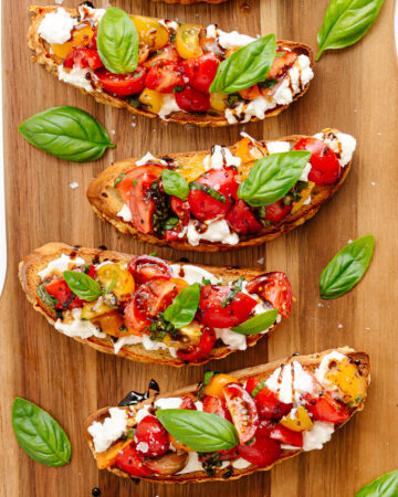 Burrata Bruschetta with tomato basil topping on a wooden board.