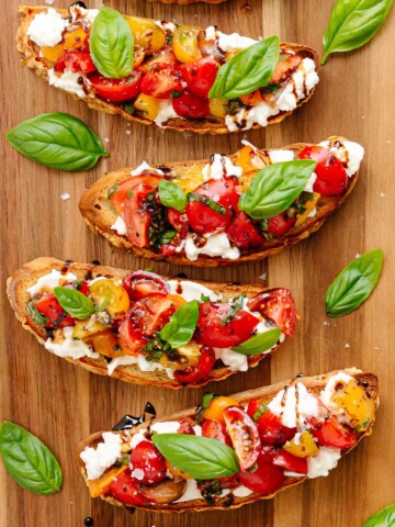 Burrata Bruschetta with tomato basil topping on a wooden board.