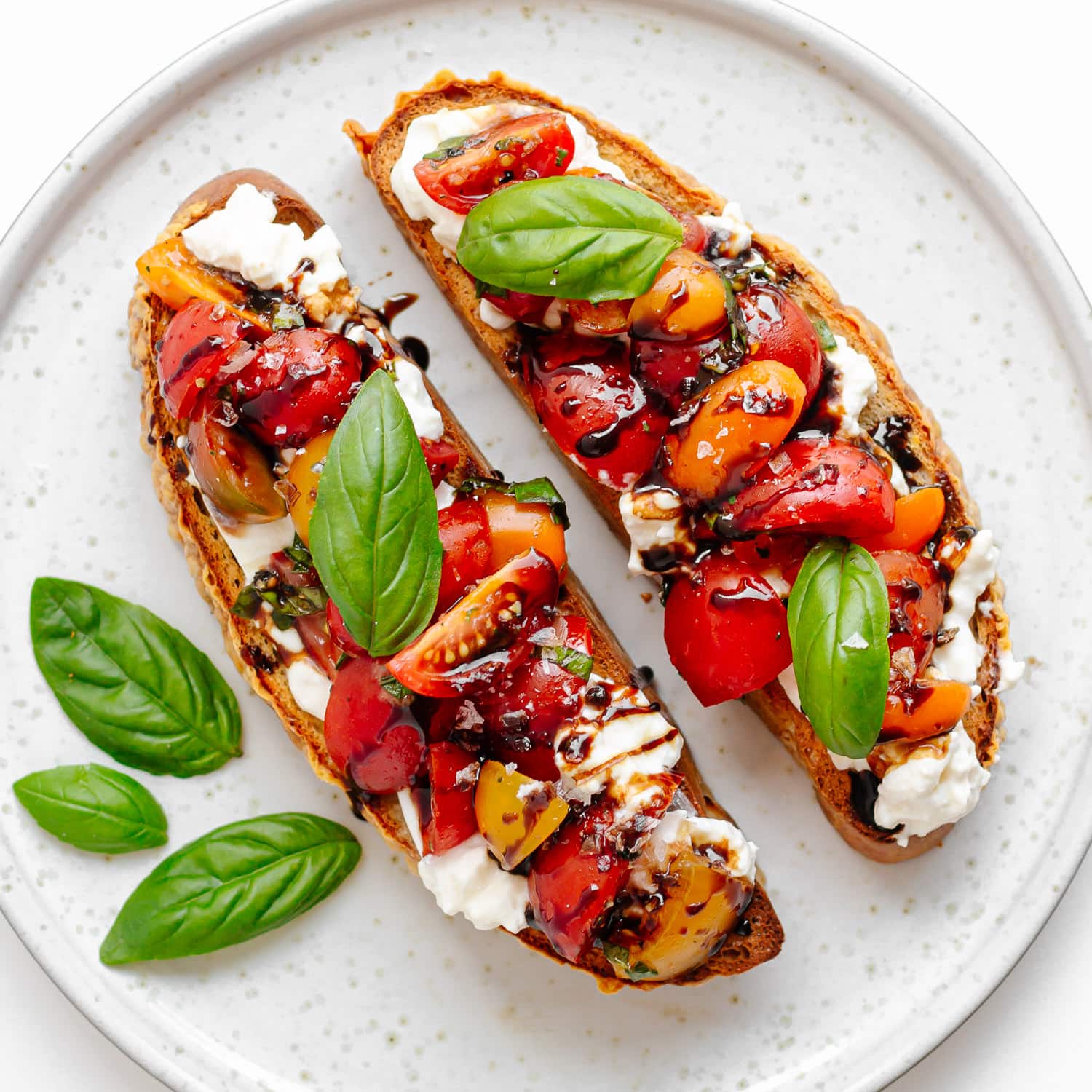 Two pieces burrata bruschetta with marinated tomato basil topping on a plate.