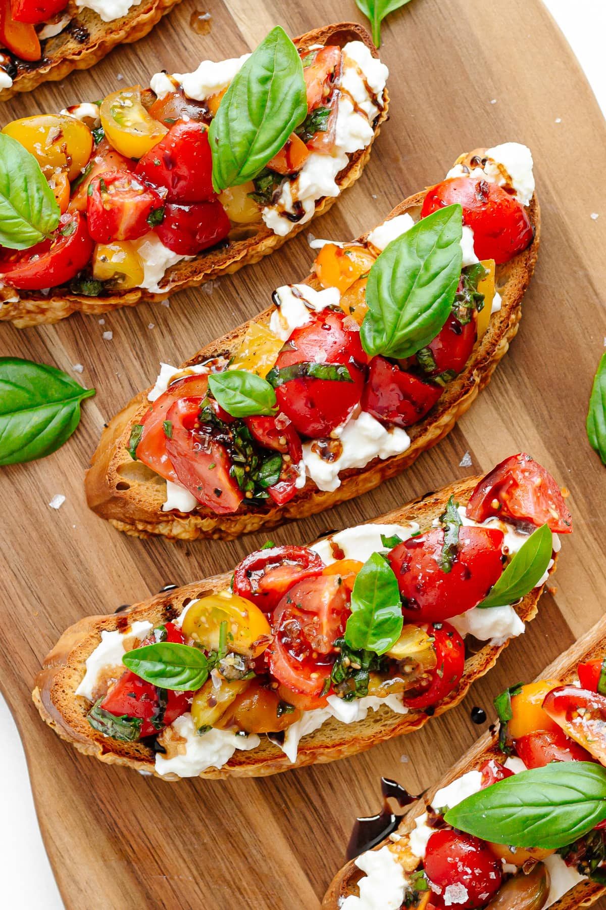 Closeup of burrata bruschetta on a wooden serving board.