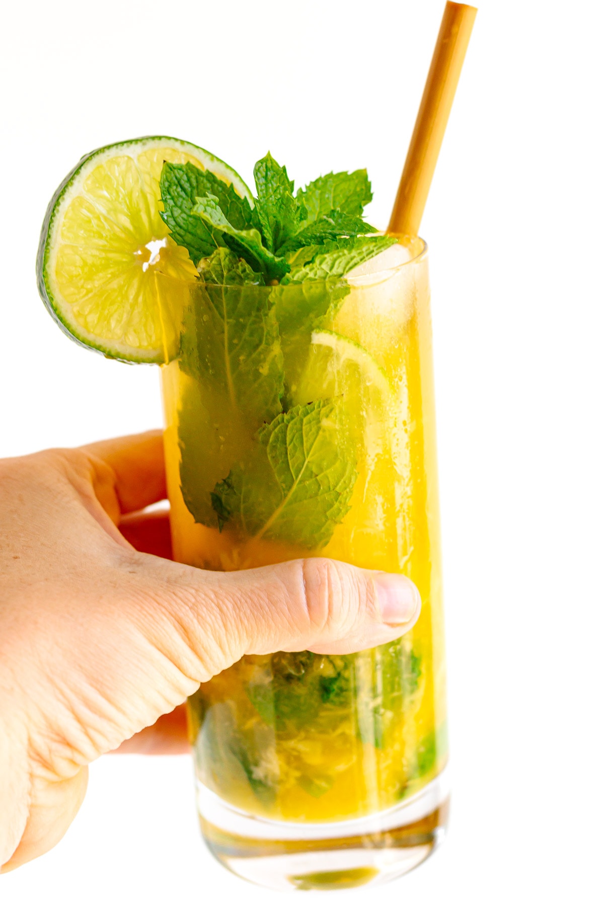 Hand holding a mango mojito garnished with fresh mint and slice of lime.
