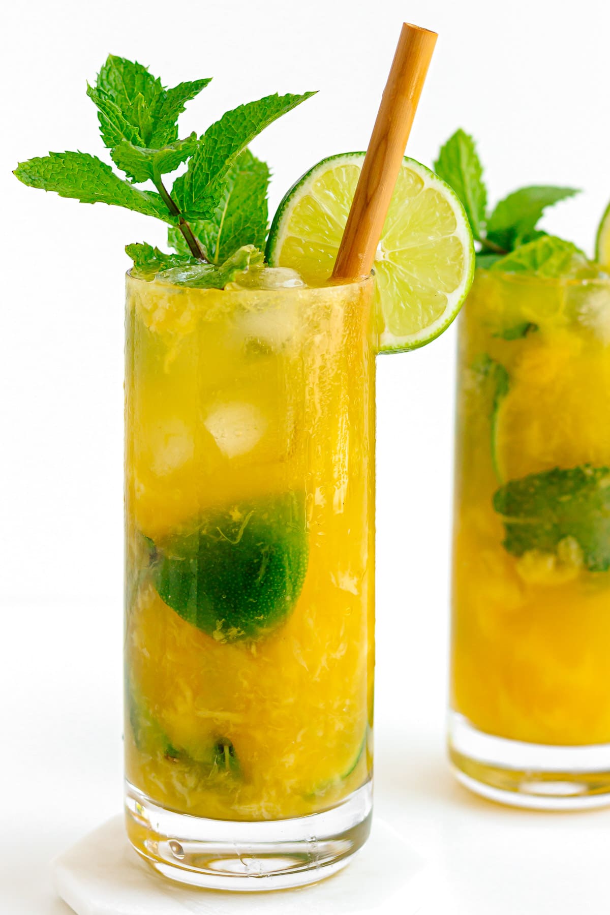 Two glasses of mango mojito cocktail garnished with fresh mint and slice of lime.