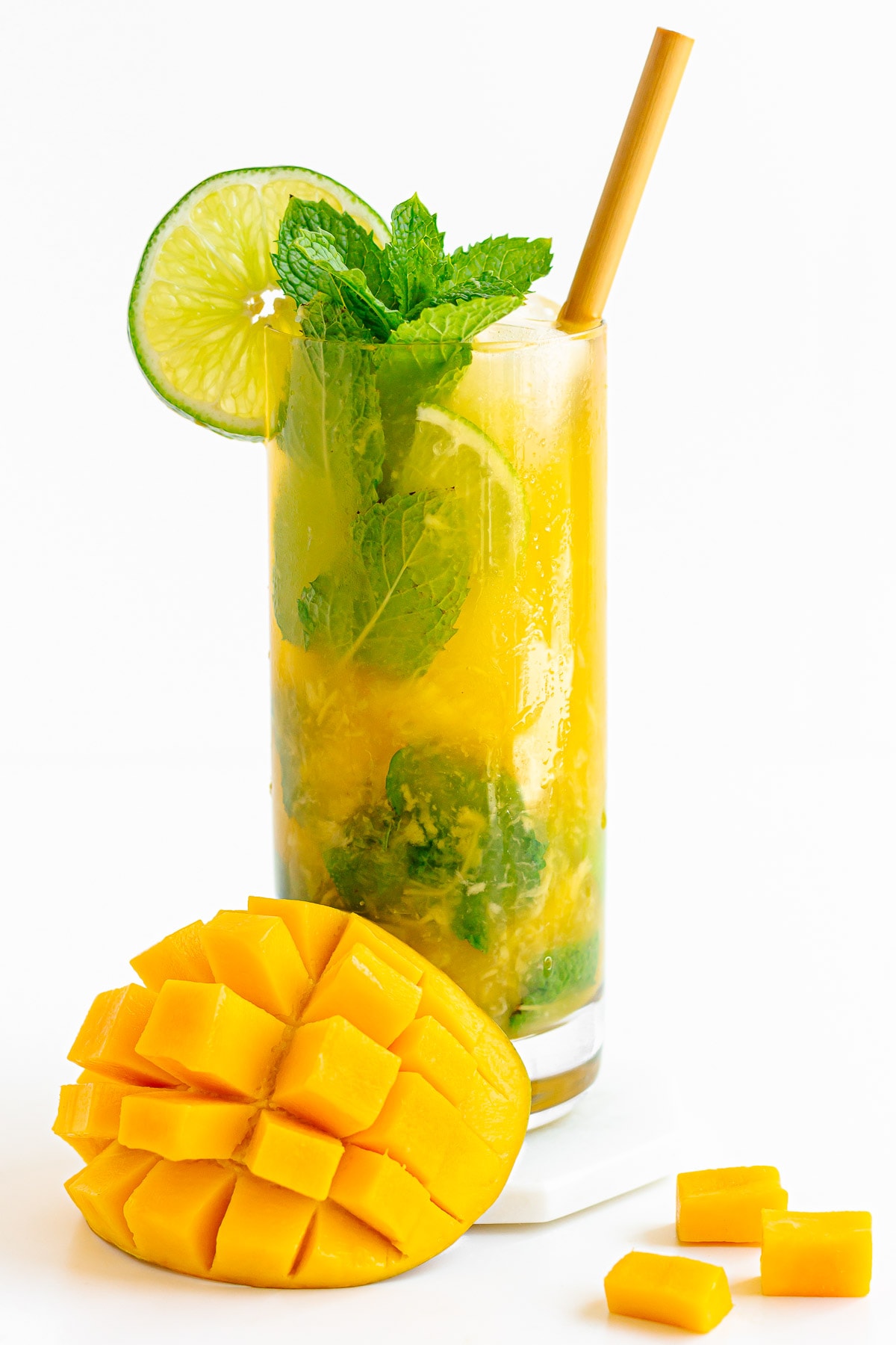 Tall glass of mango mojito with cut mango sitting next to it.