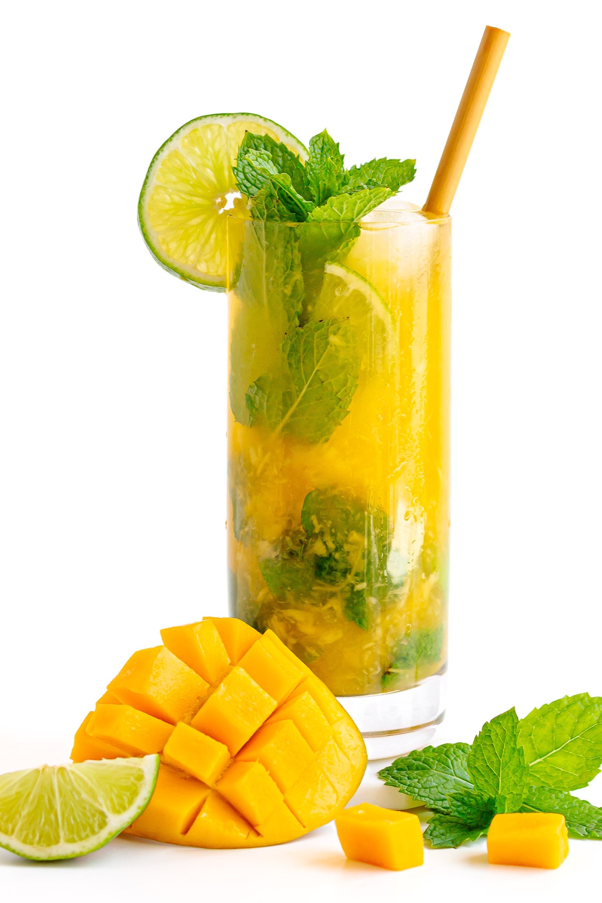 A mango mojito cocktail with mango, lime and mint sitting in front of glass.