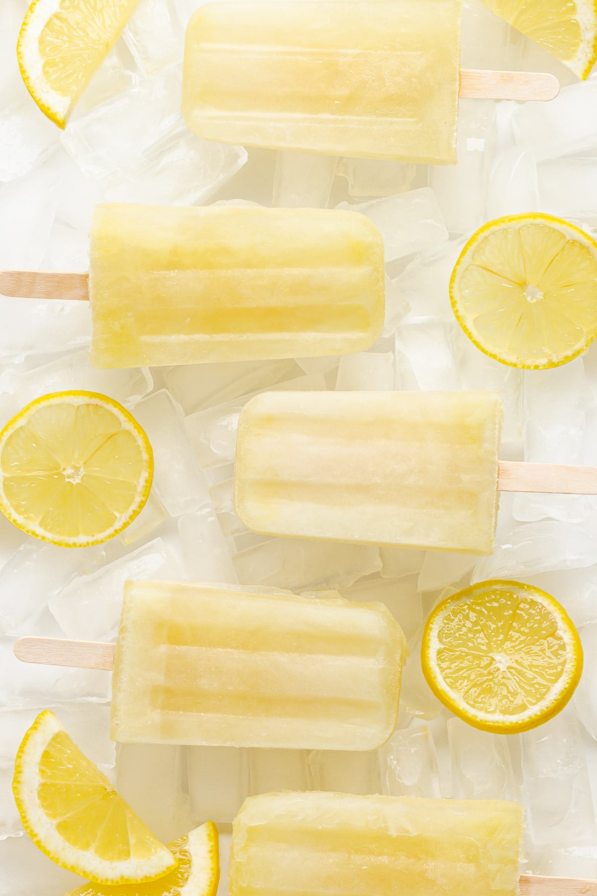 Lemonade popsicles sitting on ice with lemon slices.