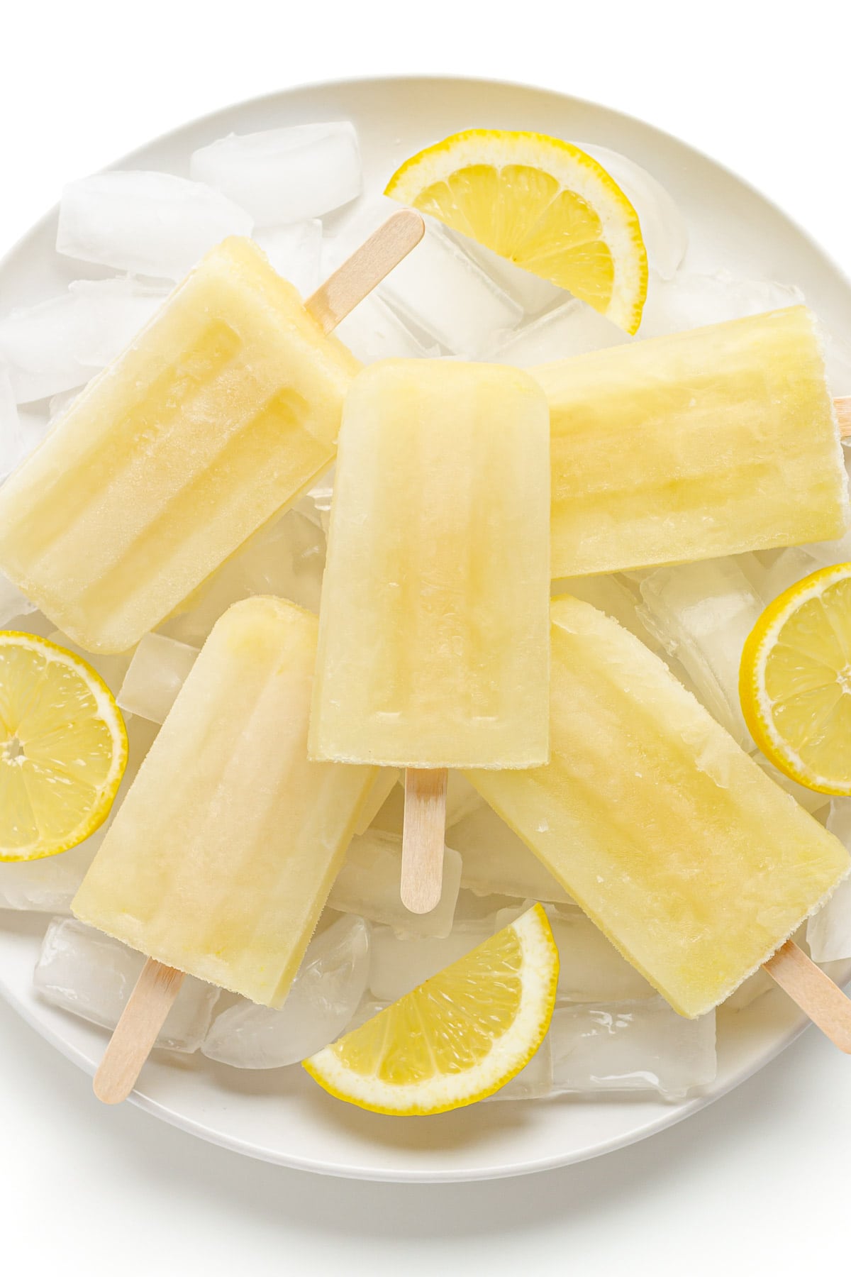 Pile of lemon popsicles on a plate of ice with lemon slices.