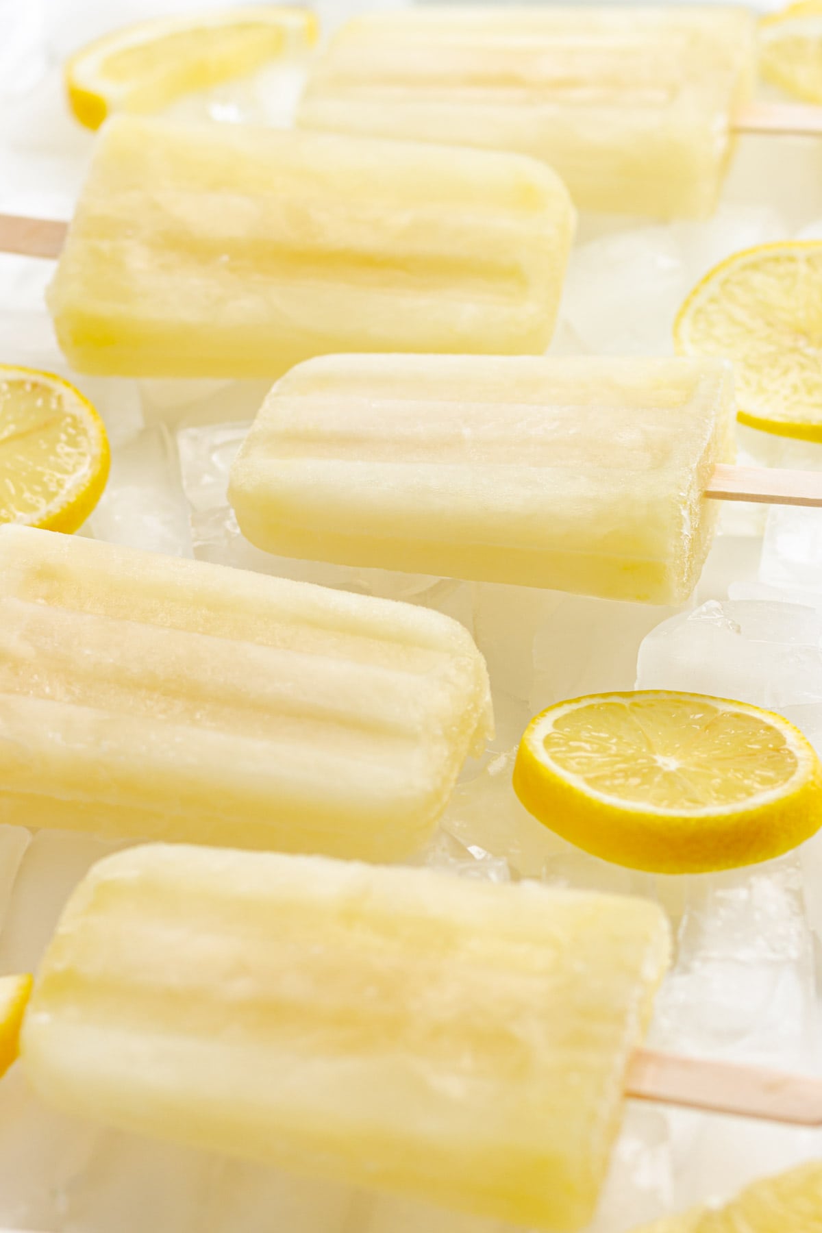 Lemonade ice pops on ice with sliced lemons.