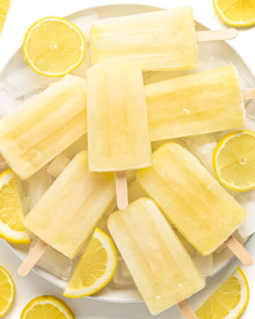 Pile of lemonade popsicles on a plate of ice surrounded by lemon slices.