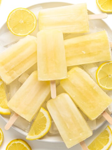 Pile of lemonade popsicles on a plate of ice surrounded by lemon slices.