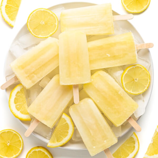 Pile of lemonade popsicles on a plate of ice surrounded by lemon slices.