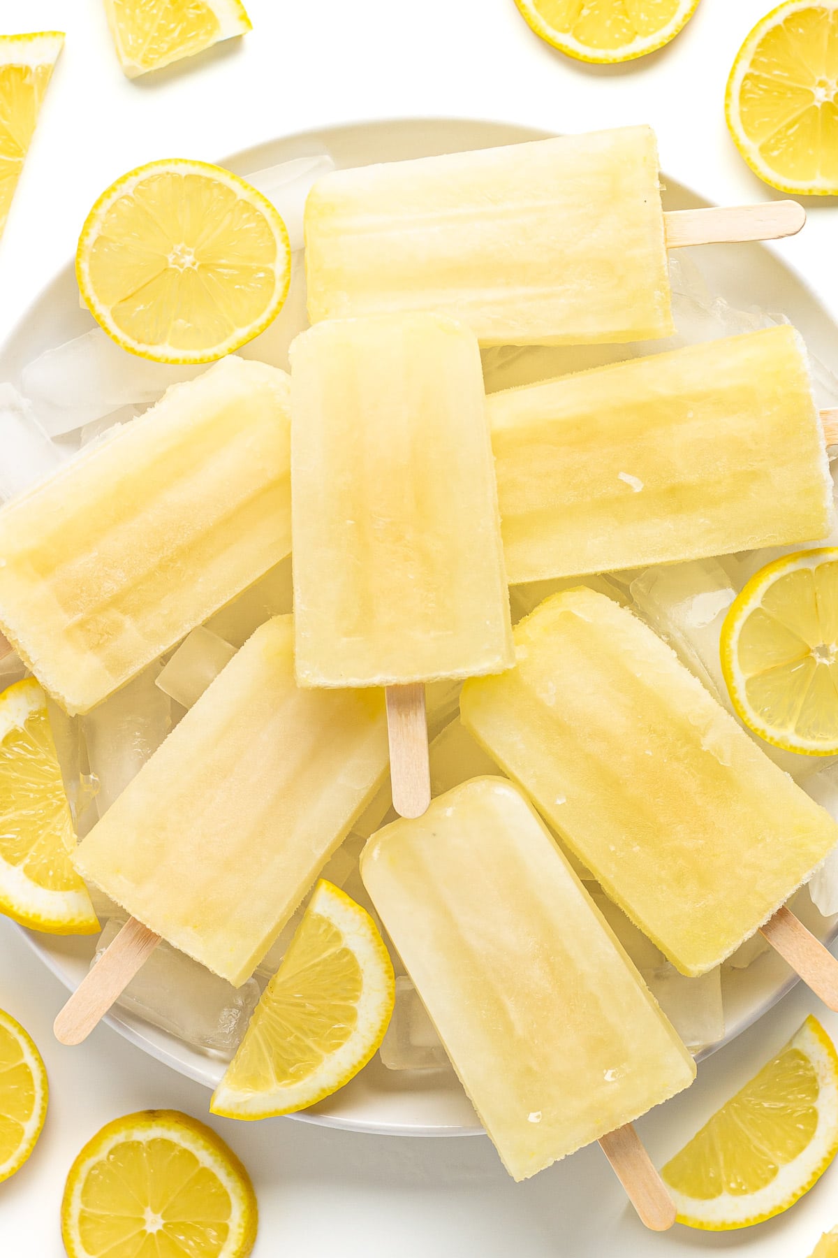 Plate of lemonade popsicles sitting on ice surrounded by sliced lemons.