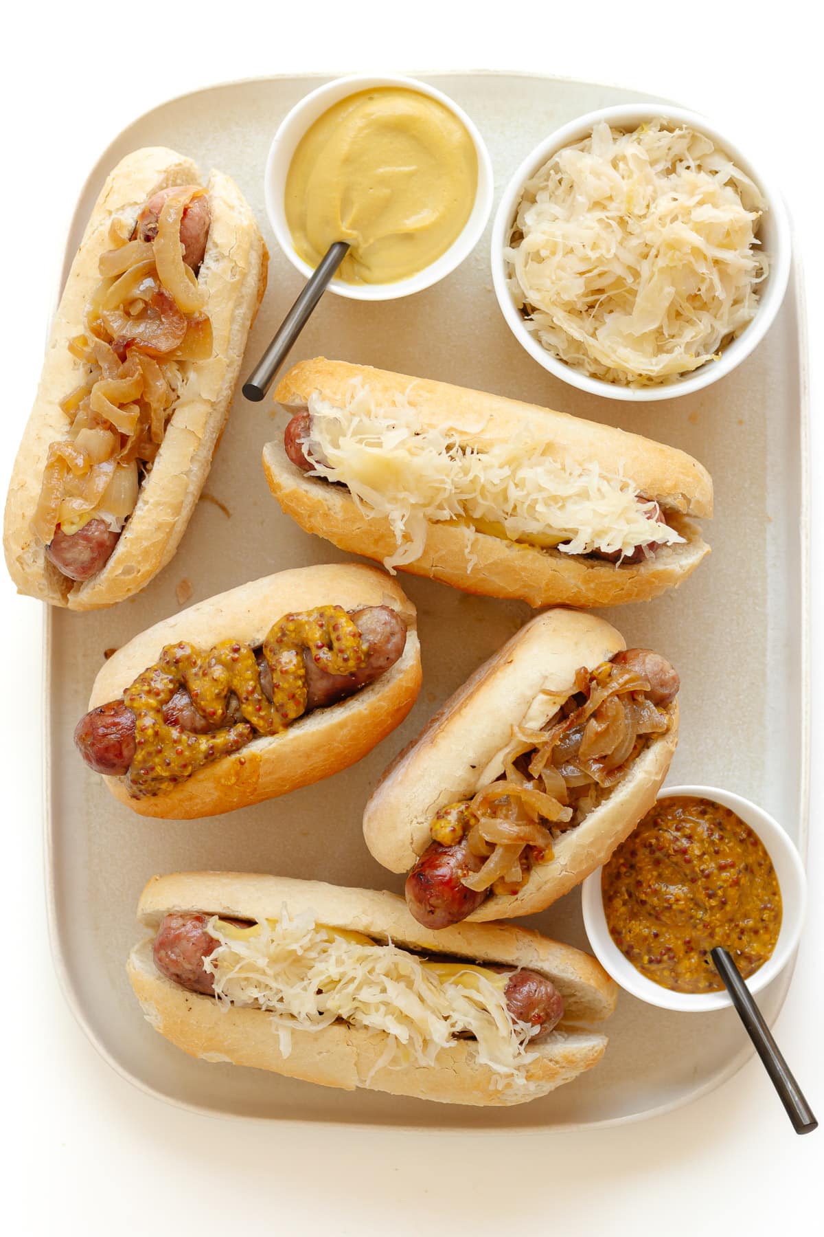 Platter of bratwurst in buns with various toppings.