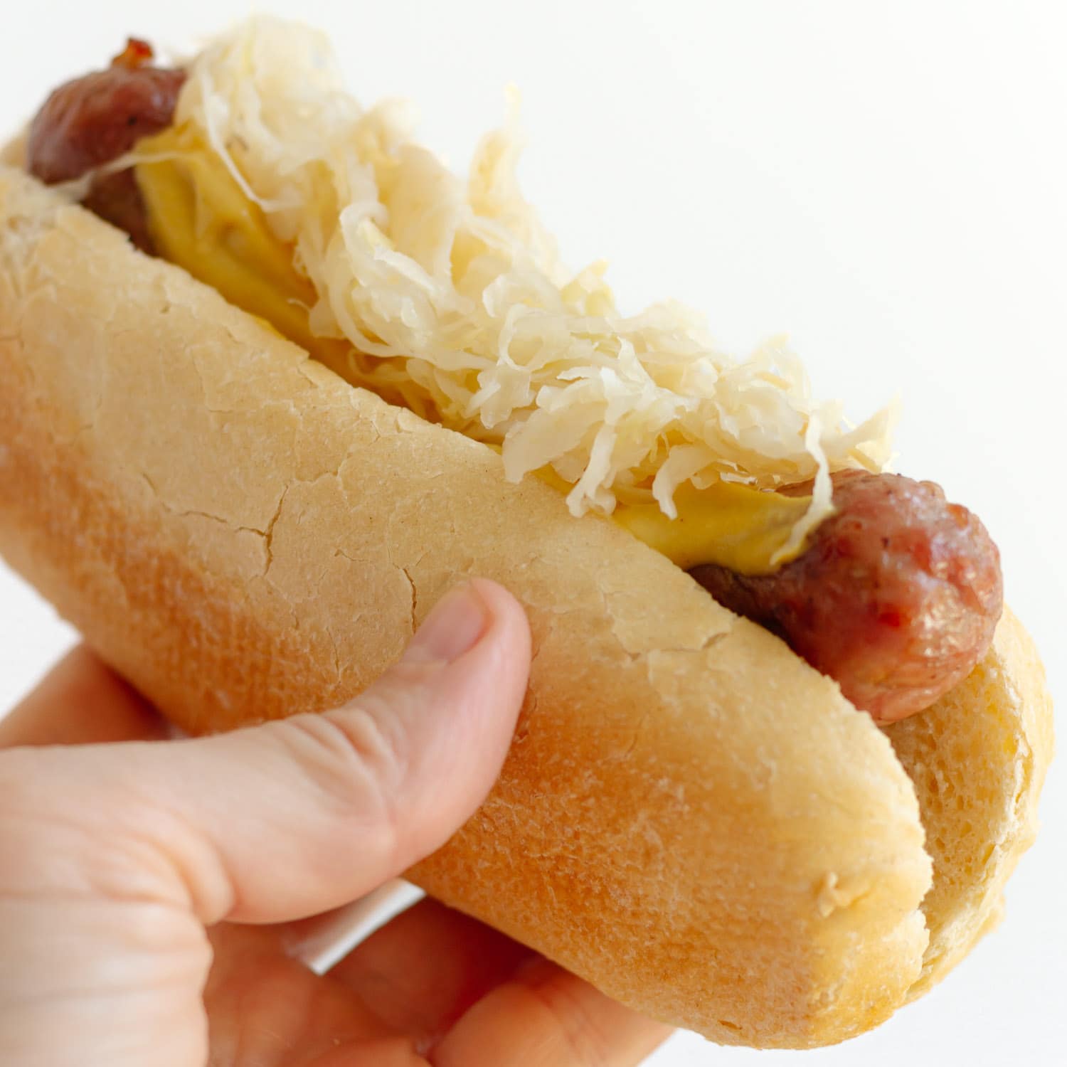 Hand holding bratwurst on a bun topped with mustard and sauerkraut.
