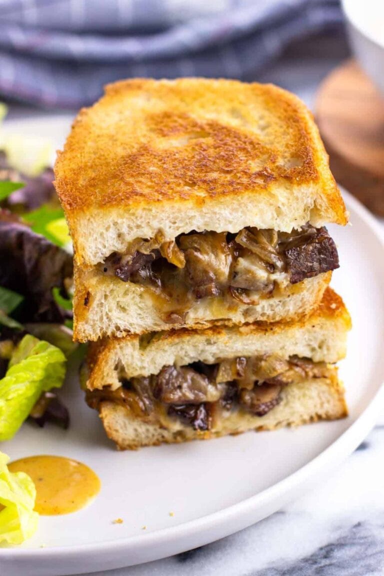 Steak sandwich on a plate with a side salad.