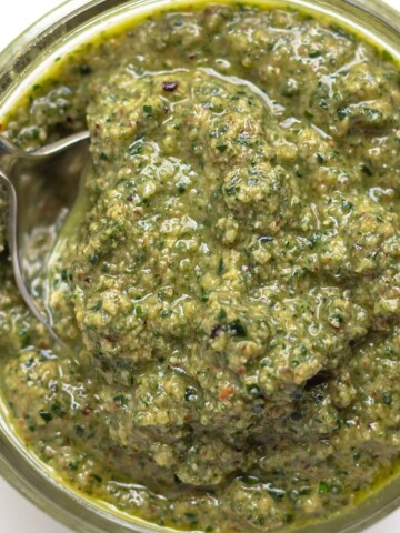 Spoon scooping sage pesto out of a small glass jar.