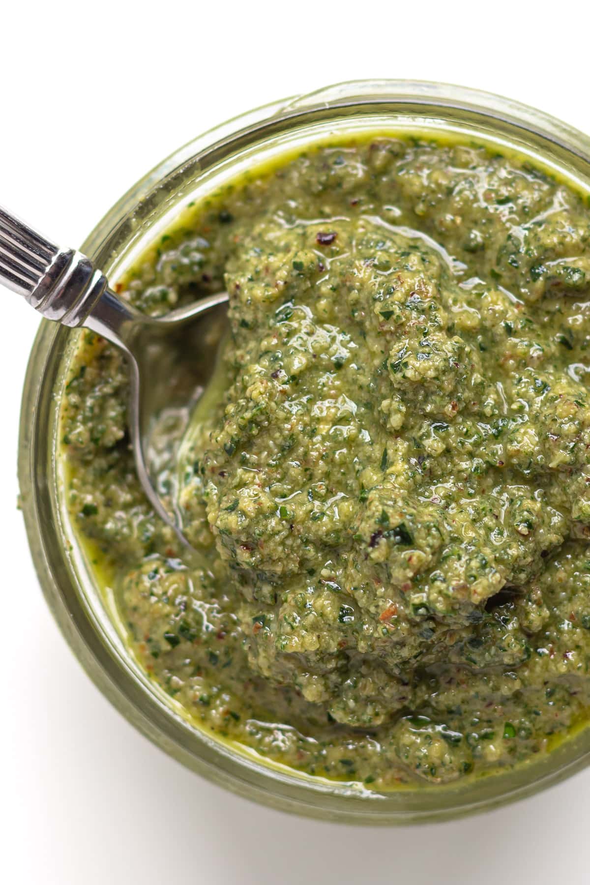 Glass jar of sage pesto with spoon scooping some out.