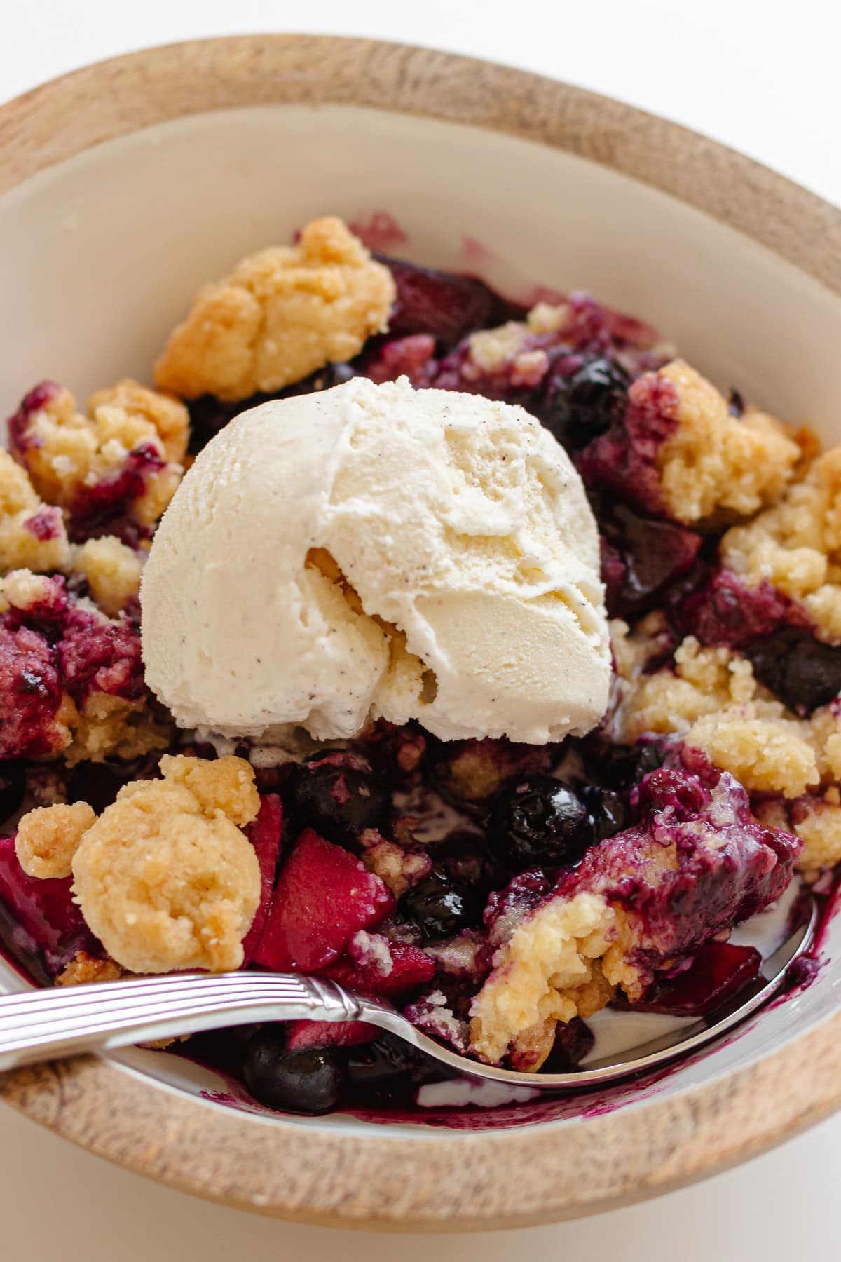 Bowl of apple and blueberry crumble with a scoop of vanilla ice cream on top.