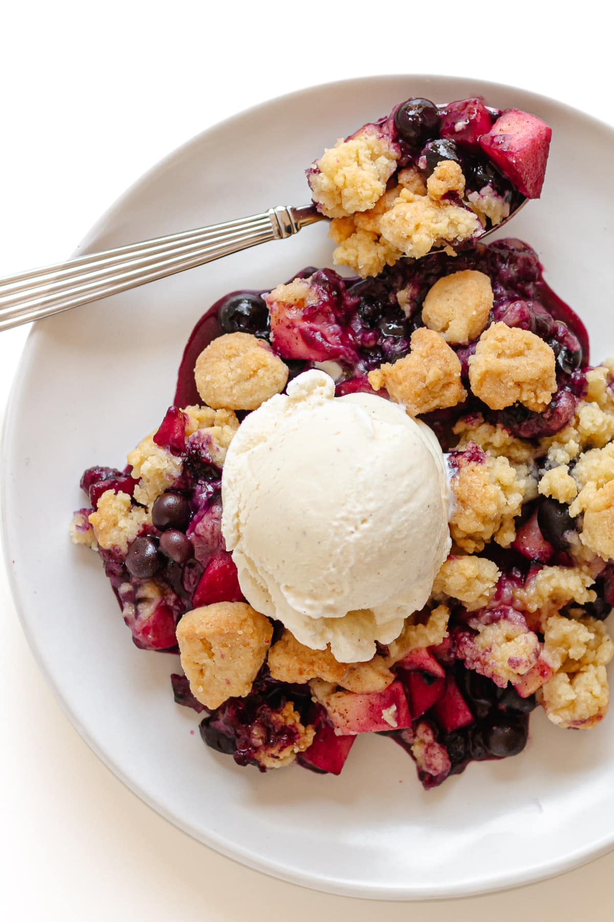 Blueberry and apple crumble on a white serving plate with scoop of vanilla ice cream.