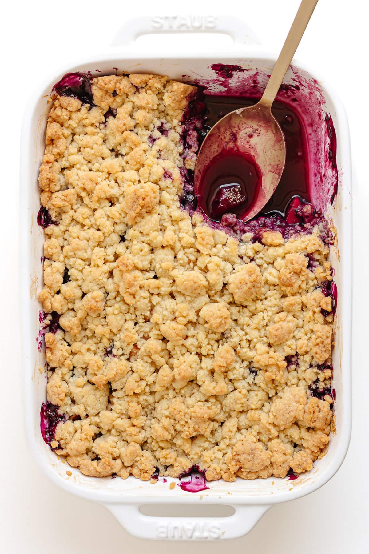 White baking dish of blueberry and apple crumble with a section scooped out of the top right corner.