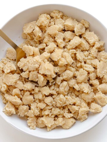 Unbaked butter streusel topping in a white bowl with gold serving spoon.