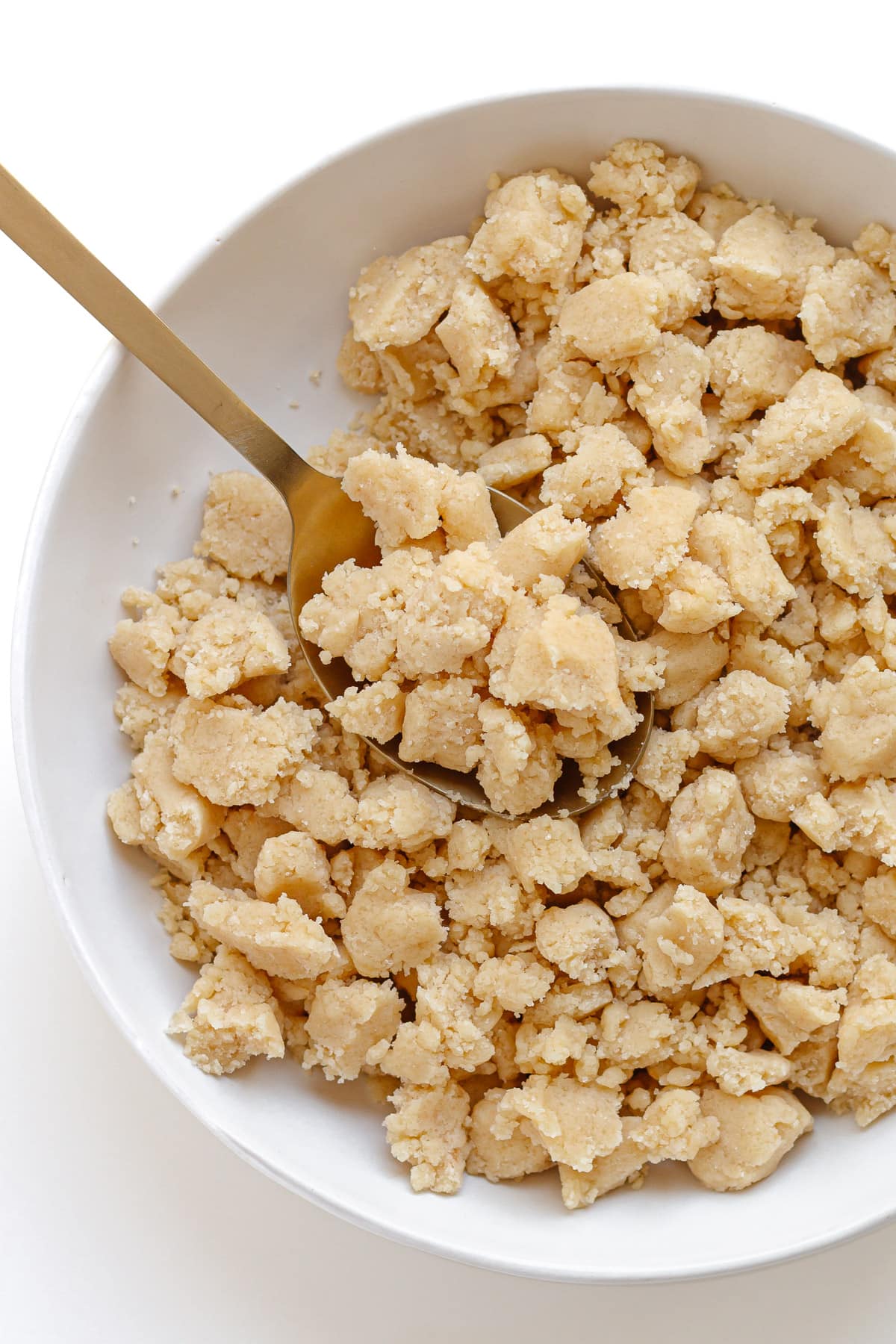 Homemade streusel topping in a white bowl with gold spoon.