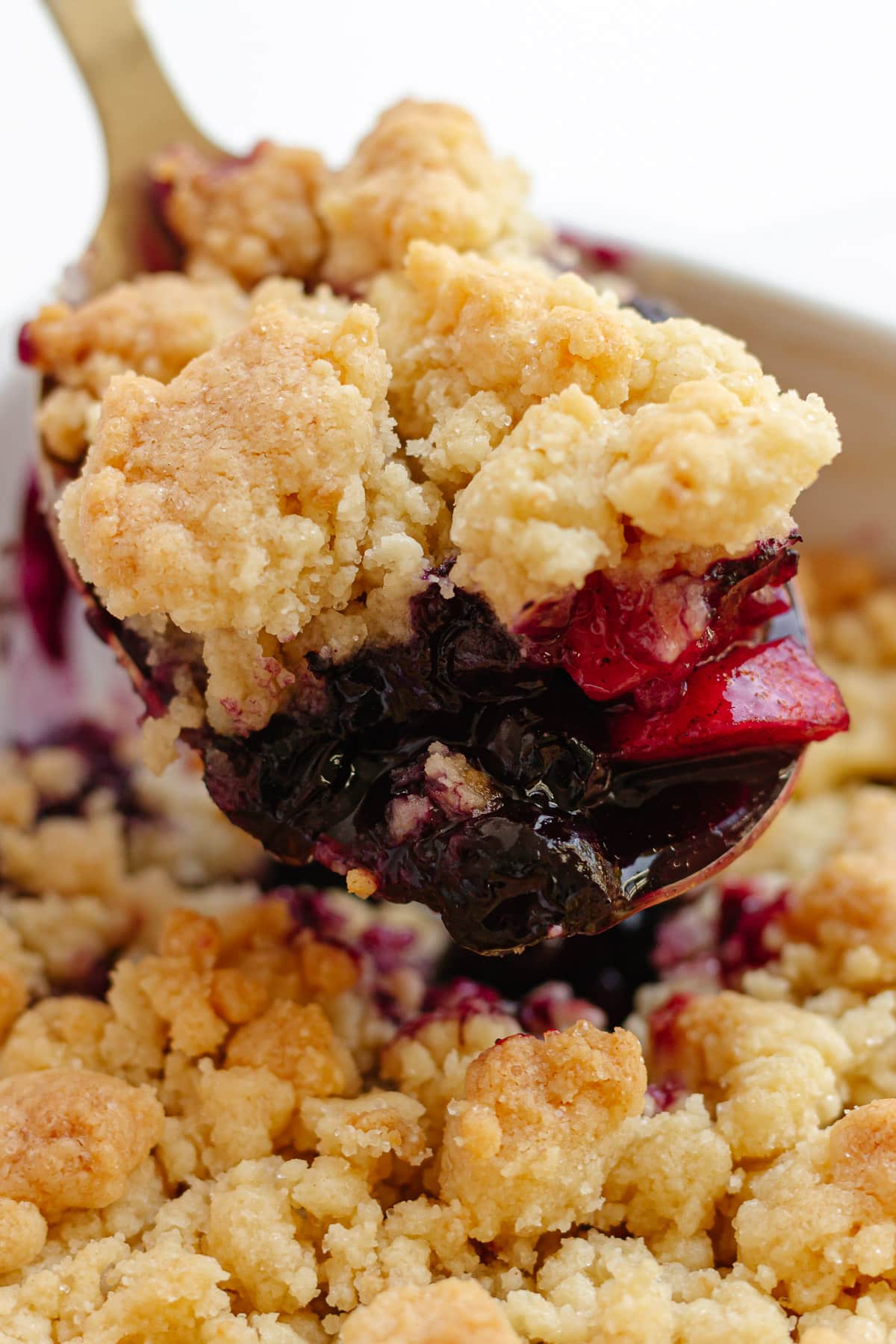 Serving spoon scooping up some apple and blueberry crumble.