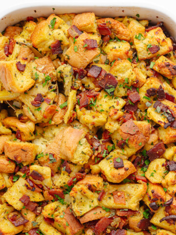 Bacon, sage and onion stuffing in a white casserole dish with serving spoon in corner.