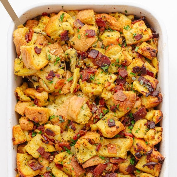 Bacon, sage and onion stuffing in a white casserole dish with serving spoon in corner.