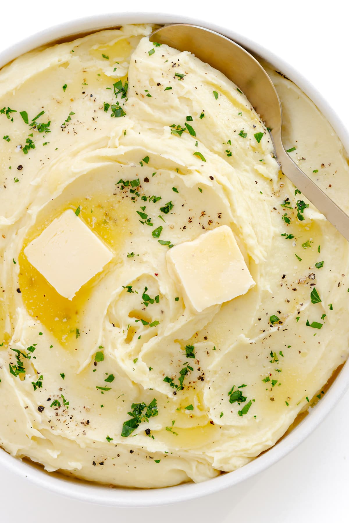 Creamy mashed potatoes in a white serving bowl with serving spoon.