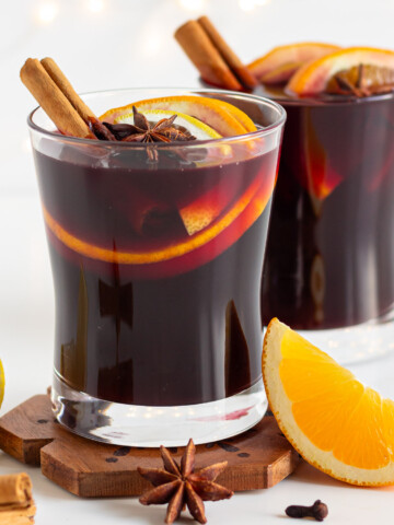 Two glasses of Gluhwein garnished with orange, cinnamon sticks and star anise.
