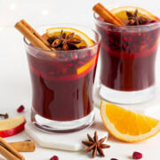 Two glasses of Kinderpunsch (non-alcoholic mulled wine) garnished with orange and apple slices, cinnamon sticks, star anise and pomegranate arils.
