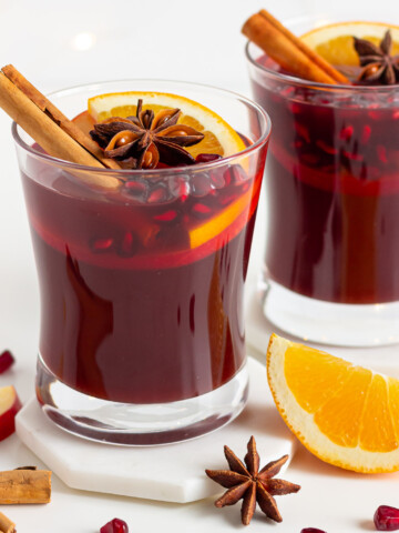 Two glasses of Kinderpunsch (non-alcoholic mulled wine) garnished with orange and apple slices, cinnamon sticks, star anise and pomegranate arils.