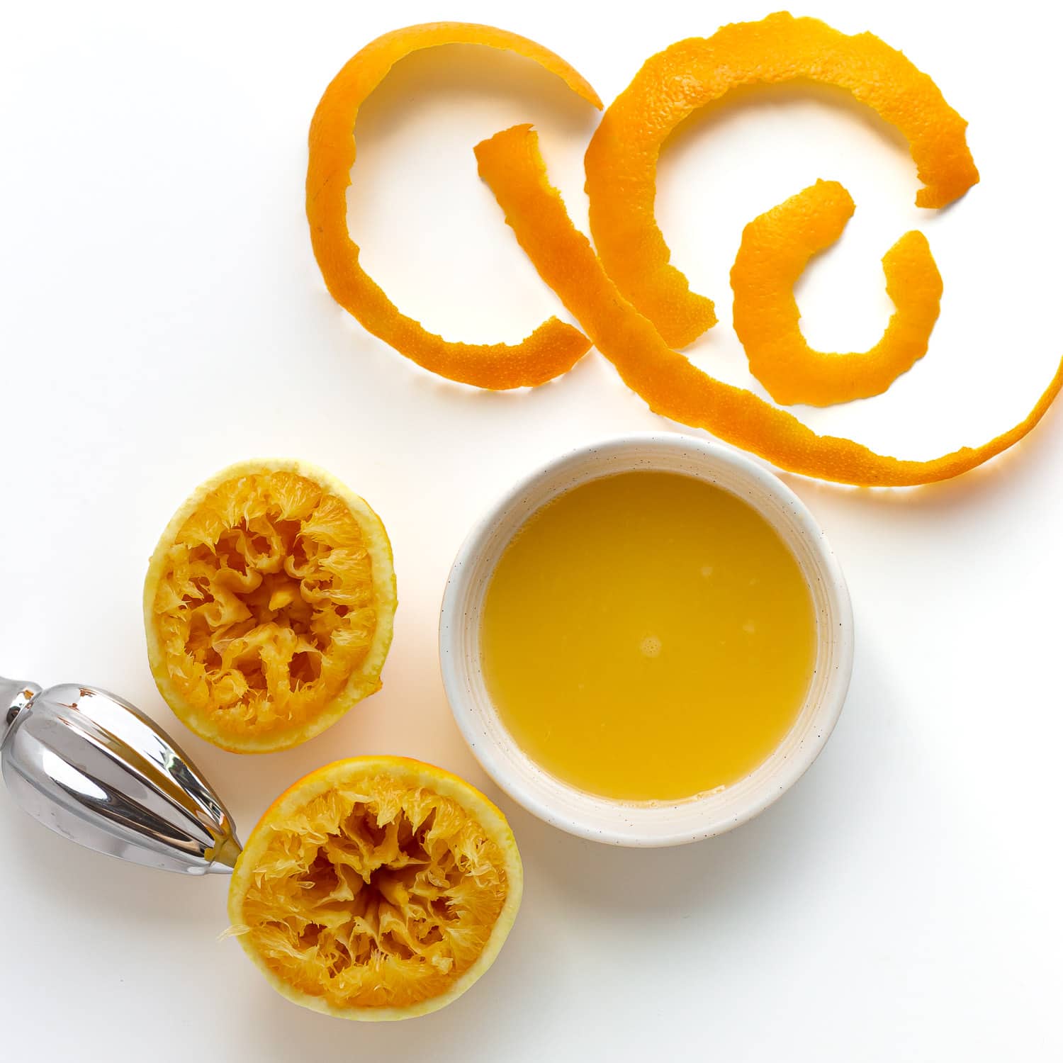 Thick strips of orange zest, bowl of orange juice and the remaining orange halves.