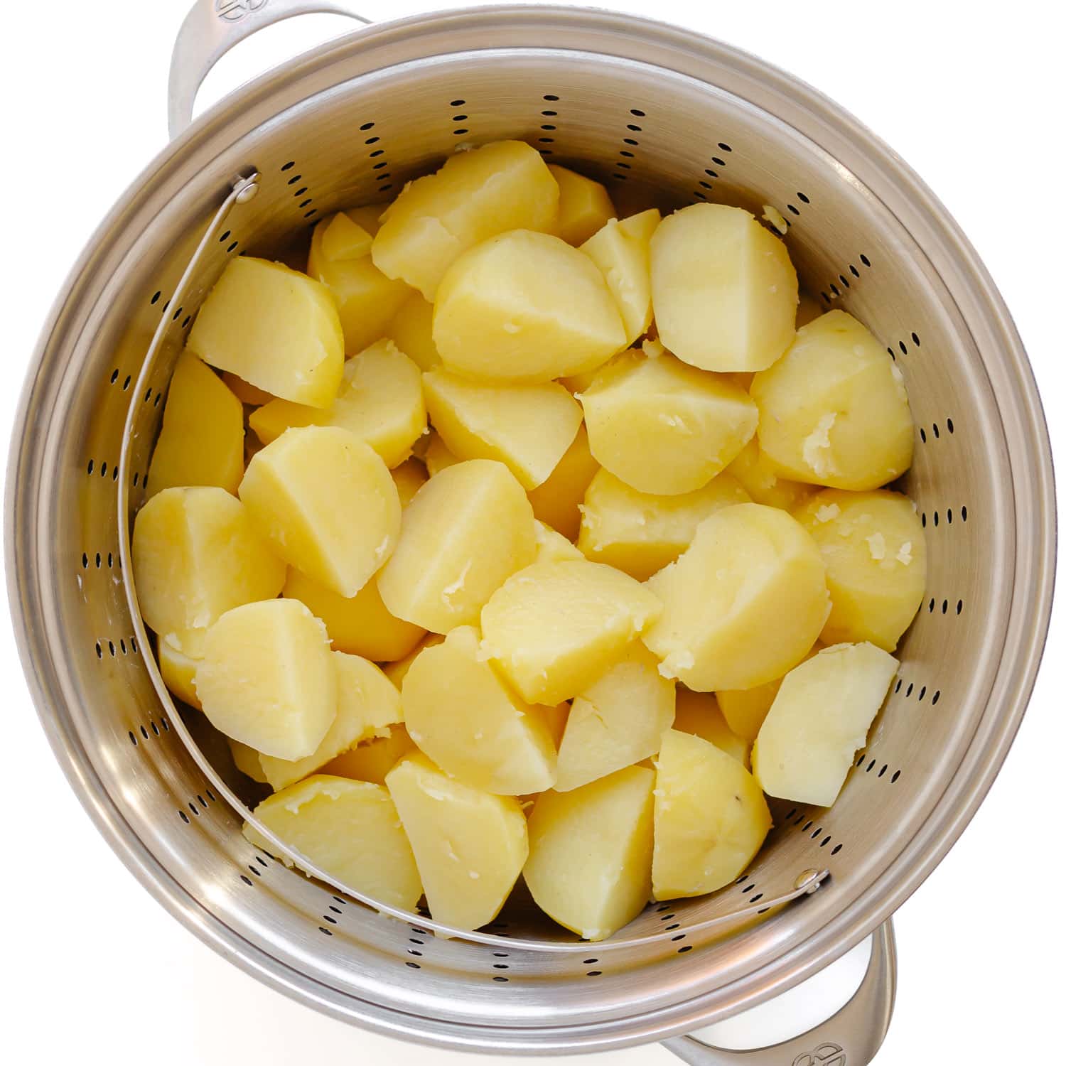 Peeled and cut up steamed potatoes in a steamer basket insert in stockpot.