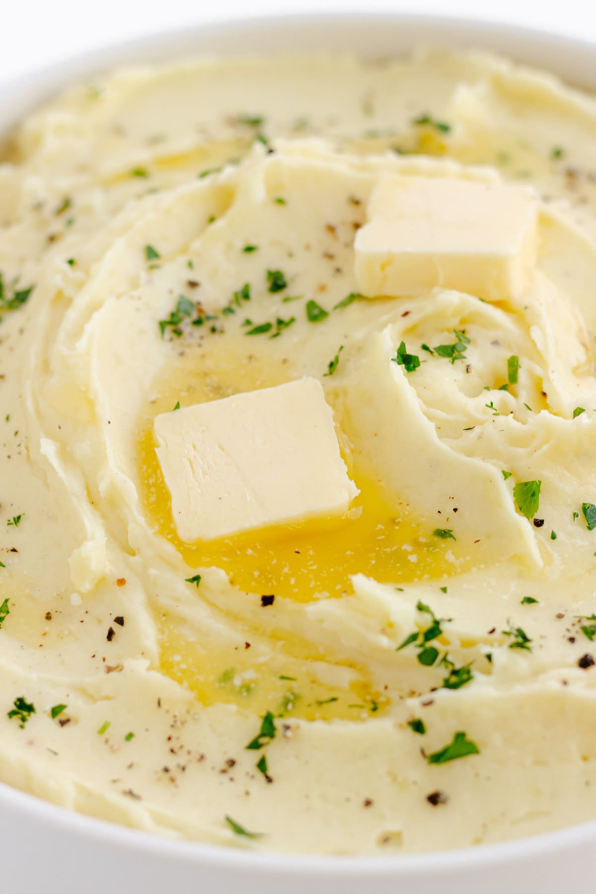 Whipped potatoes with pats of butter melting on top, chopped parsley and black pepper.