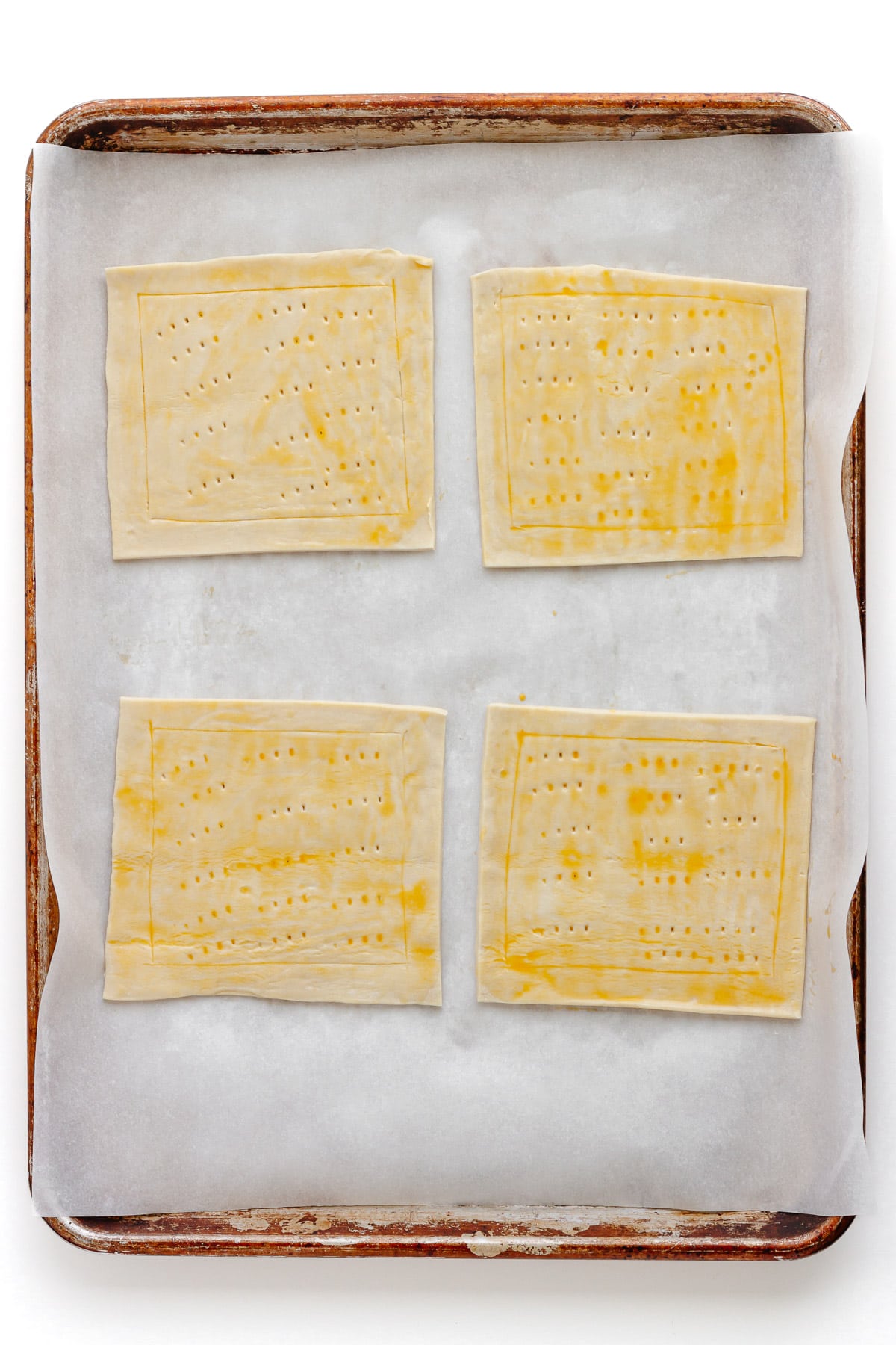 Four squares of puff pastry on a lined baking sheet ready to be prebaked.