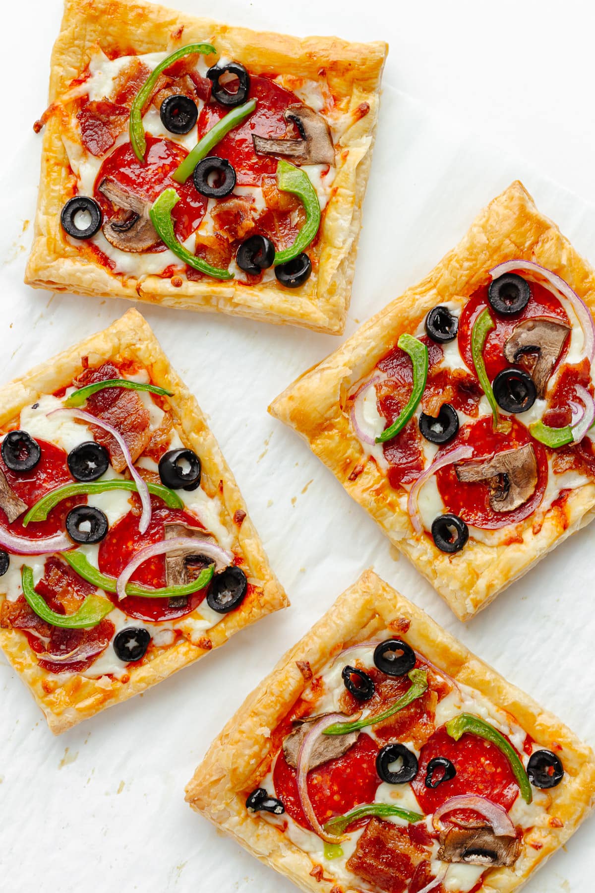 Four square pieces of puff pastry pizza on parchment paper.