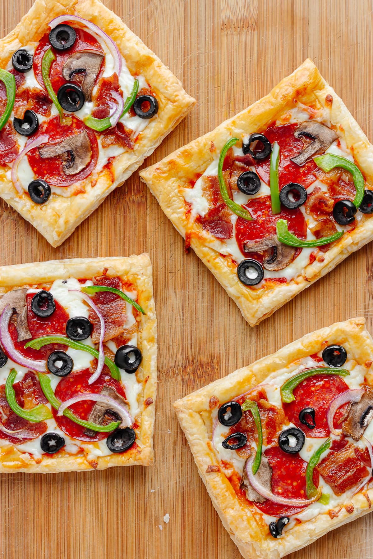 Four square pizzas on puff pastry sitting on a wooden serving board.