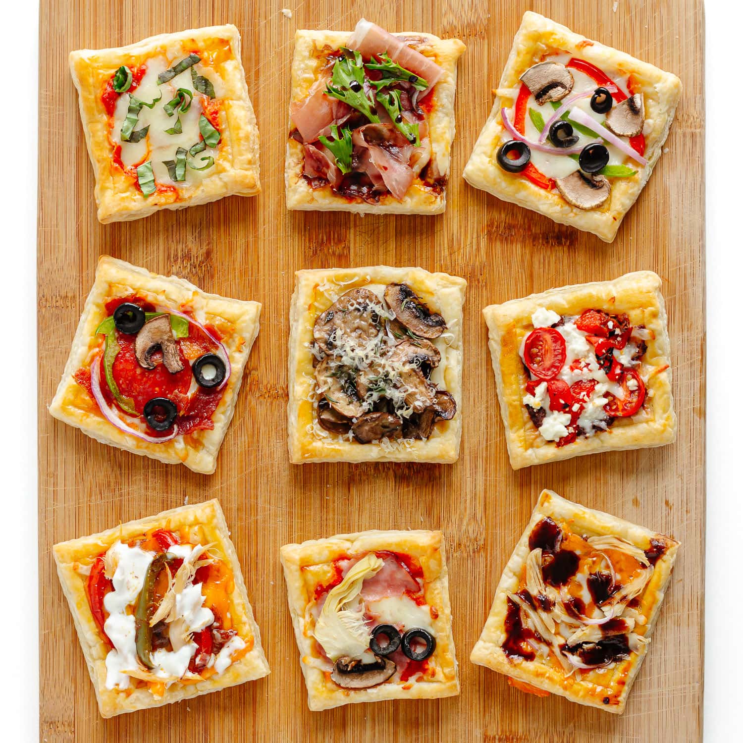 Variety of puff pastry pizza with different toppings on a wood board.