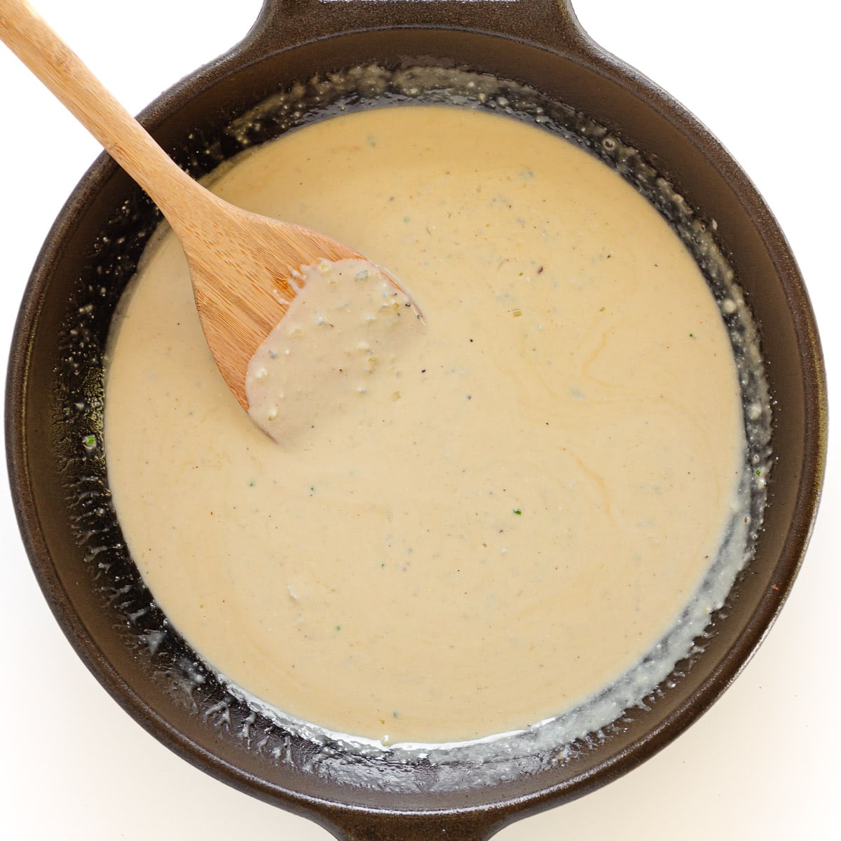 Gorgonzola cream sauce in cast iron skillet with wooden spoon.