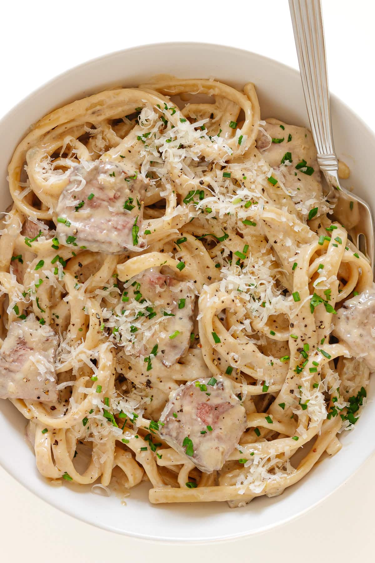 Creamy steak pasta on a white plate with fork.