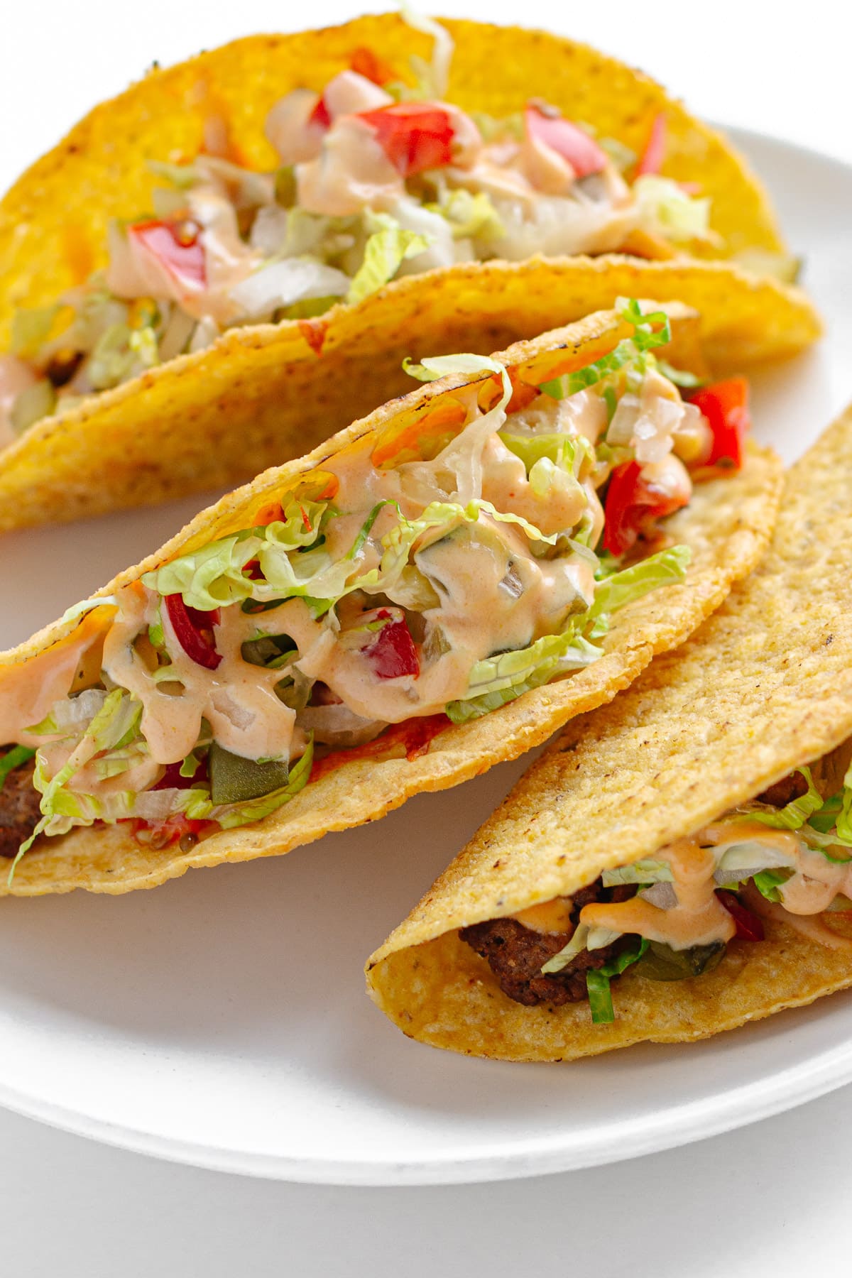 Three cheeseburger tacos on a white plate.