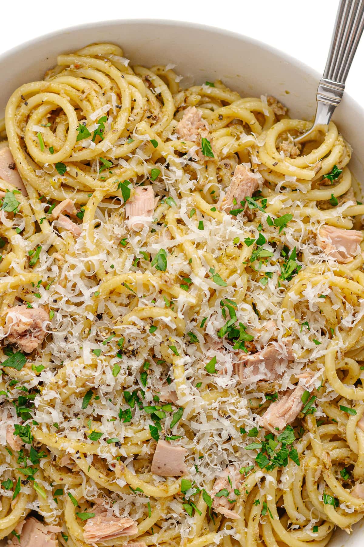 Closeup of pesto and tuna spaghetti garnished with grated Parmesan and chopped parsley.
