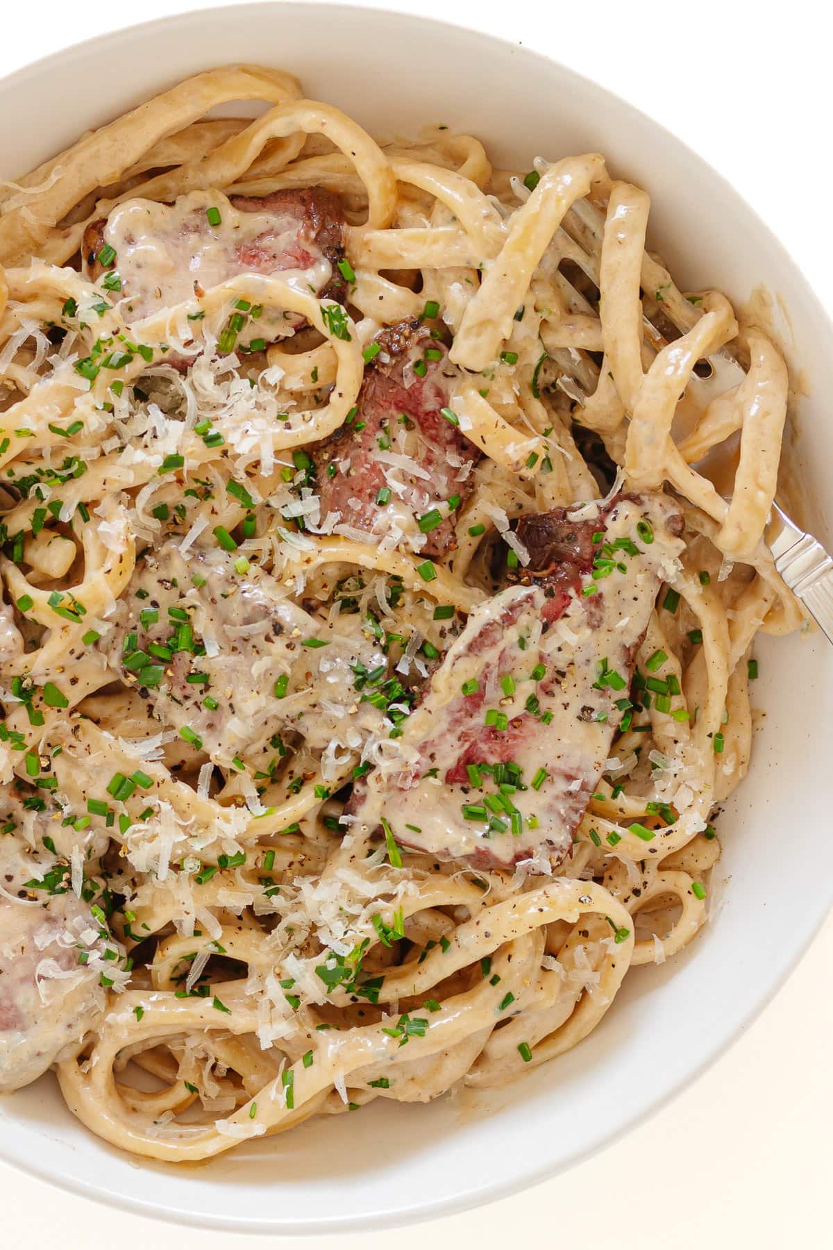 Gorgonzola pasta with steak on a white plate with fork.