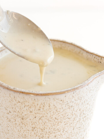 Small sauce pitcher of gorgonzola sauce with spoon lifting some out.