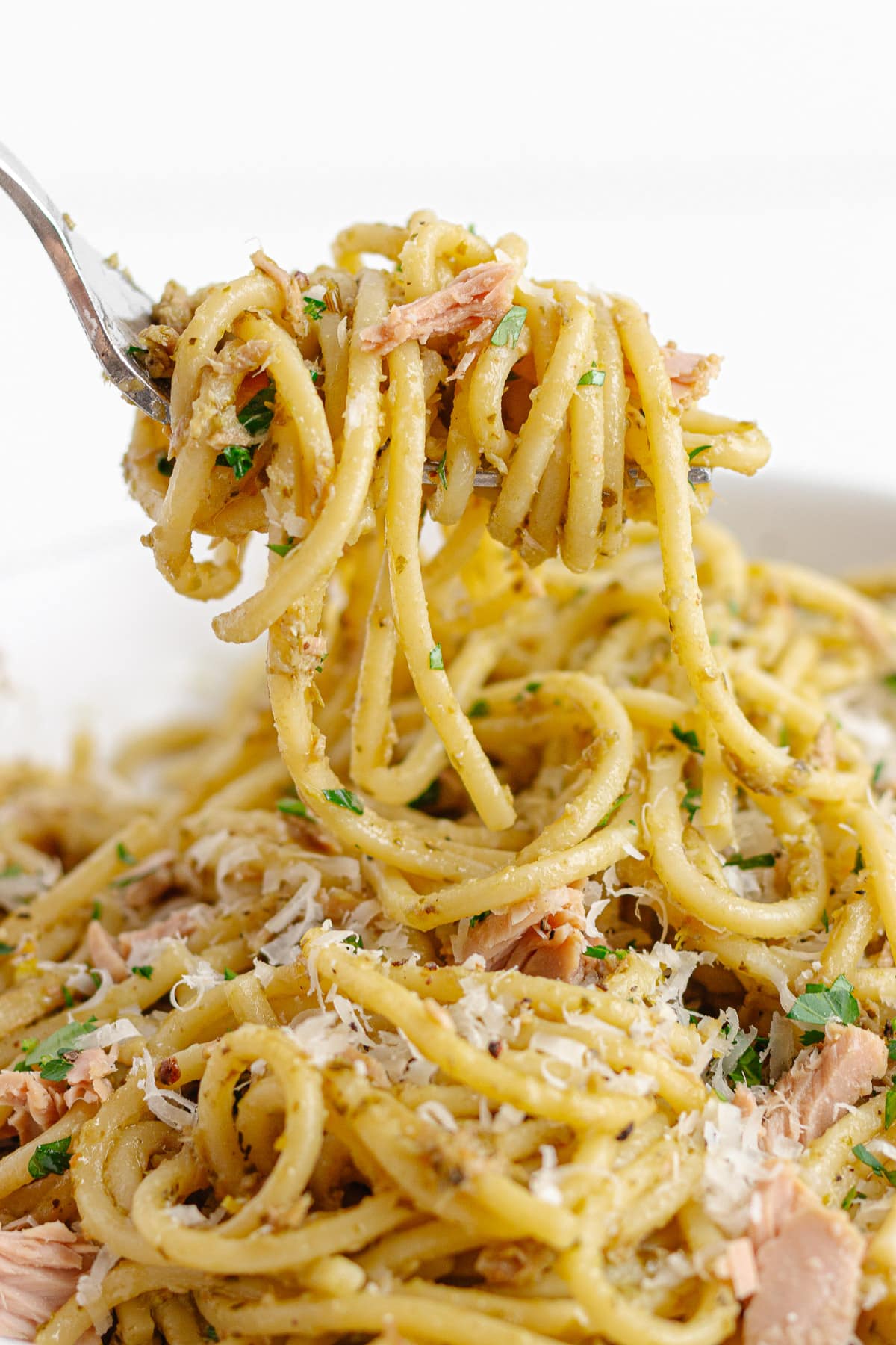 Fork lifting up spaghetti with pesto and tuna.