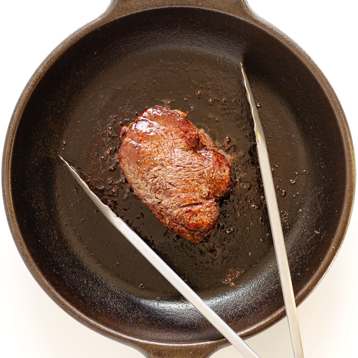 Filet mignon searing in a cast iron skillet.
