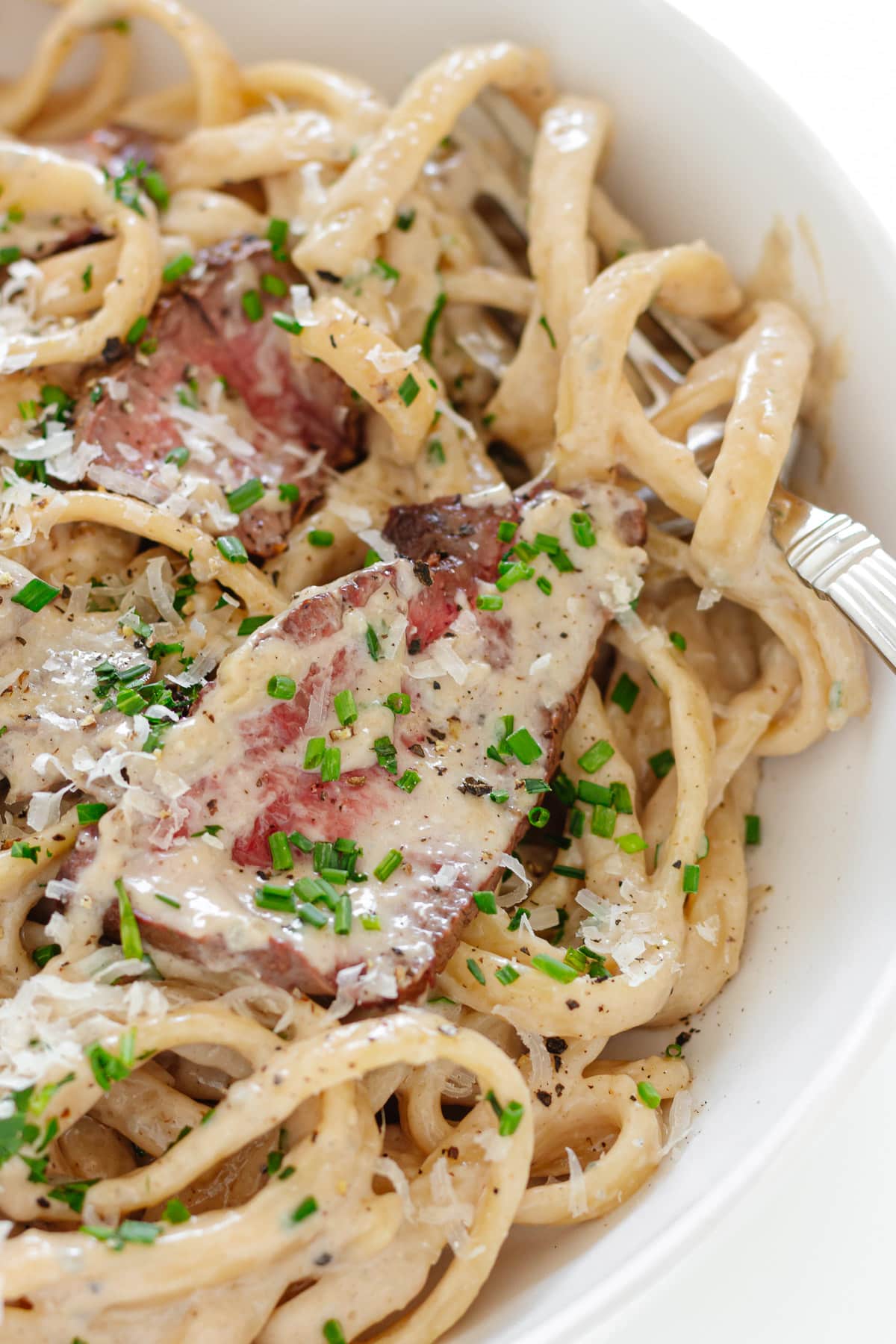 Steak pasta with creamy gorgonzola sauce on a white plate with fork.